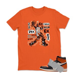 May include: Orange t-shirt with a graphic of a basketball player in action, flames, and text. The text includes "23", "6X Finals", "MVP", "6X", "14X NBA All-Star". A black, white, and orange high-top sneaker is in the foreground.