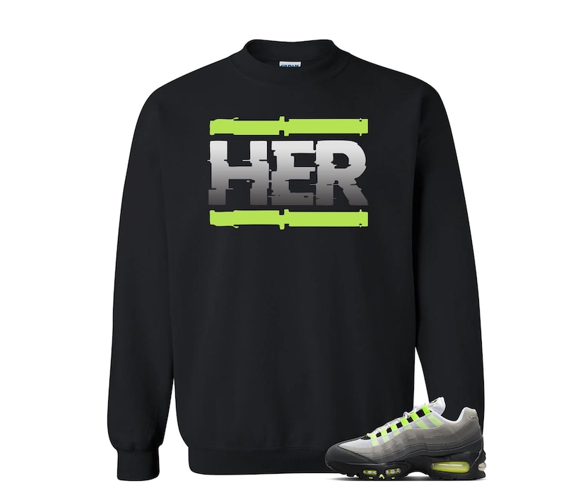 Pu&ograve; includere: Felpa nera con la scritta "HER" in un font in stile glitch, accentuata da linee orizzontali verde neon. Un paio di scarpe da ginnastica grigie, nere e verde neon sono in primo piano.