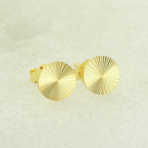 Puede incluir: Un par de pendientes de botón dorados con un diseño circular. Los pendientes tienen una superficie texturizada.