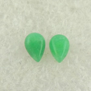 Op de afbeelding: Twee groene edelstenen in druppelvorm op een wit oppervlak.