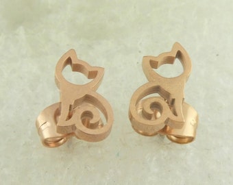 Peut inclure: Une paire de boucles d'oreilles clous en or rose en forme de silhouette de chat. Le chat est assis avec sa queue enroulée autour de son corps.