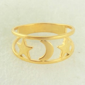 Op de afbeelding: Een goudkleurige ring met een hemels ontwerp. De ring heeft een band met een boven- en een ondergedeelte. Het onderste gedeelte heeft uitgesneden vormen van twee sterren en een halve maan. De ring is waarschijnlijk van metaal.