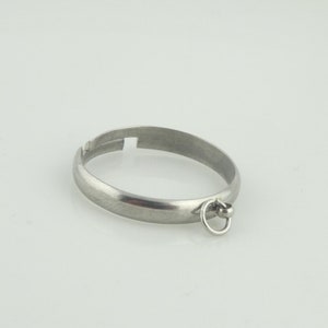 Può includere: Un anello d'argento con un piccolo anello attaccato alla parte inferiore. L'anello è aperto da un lato, il che consente di regolarlo per adattarlo a diverse dimensioni.