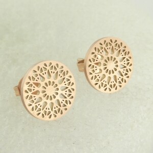 Puede incluir: Un par de pendientes de oro rosa con un diseño delicado, circular, similar a un mandala. Los pendientes están hechos de metal y tienen un acabado pulido.