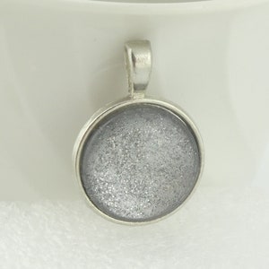 May include: A silver pendant with a round, clear glass cabochon filled with silver glitter.