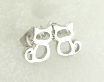 Peut inclure: Une paire de boucles d'oreilles à clous argentées en forme de chat. Chaque boucle d'oreille présente un motif découpé d'un chat avec une tête, un corps et une queue enroulée. Les boucles d'oreilles sont petites et probablement en métal.