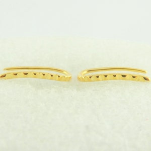 Può includere: Un paio di orecchini a cerchio in oro con un design testurizzato. I cerchi sono curvi e hanno uno stile semplice e minimalista.