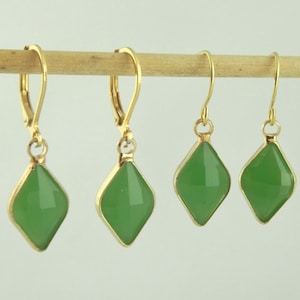 Puede incluir: Cuatro pares de pendientes colgantes de oro con detalles de piedras preciosas verdes. Los pendientes presentan una piedra preciosa en forma de diamante con un engaste de oro.