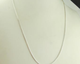 Puede incluir: Un delicado collar de plata exhibido sobre un maniquí blanco. La cadena es fina y parece estar hecha de pequeños eslabones interconectados. El collar está drapeado en una curva suave, mostrando su simple elegancia.