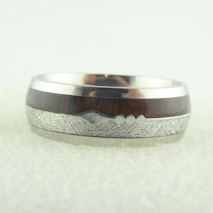 Könnte beinhalten: Ein silberner und brauner Ring mit einer Holzeinlage und einem strukturierten Silberband.
