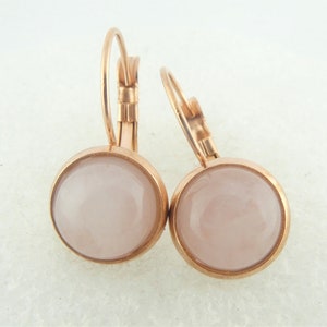 Op de afbeelding: Een paar rose gouden oorringen met een lichtroze cabochon-steen in elke oorring.