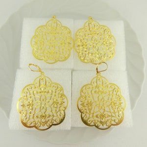 Könnte beinhalten: Vier goldfarbene Filigranohrringe. Zwei werden als einzelne Anhänger und zwei mit Ohrhaken präsentiert. Die Ohrringe haben ein florales, offenes Design. Die Ohrringe werden auf weißem Schaumstoff präsentiert.
