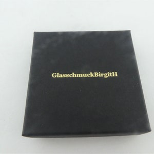May include: Black box with the text "GlassmuckBirgitH" in gold lettering.