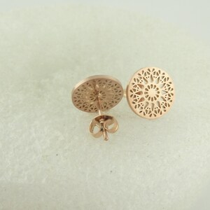 May include: A pair of rose gold earrings with a delicate, circular, openwork design. The earrings are made of metal and have a post-back closure.
