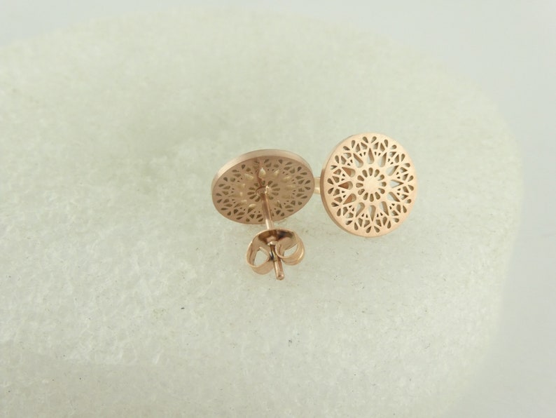 May include: A pair of rose gold earrings with a delicate, circular, openwork design. The earrings are made of metal and have a post-back closure.