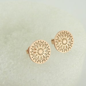 May include: A pair of rose gold earrings with a circular, intricate, cut-out design.