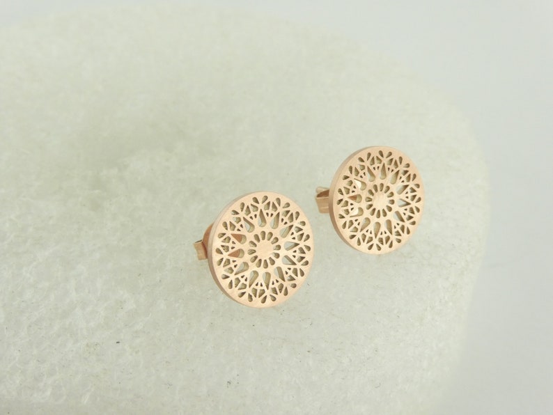 May include: A pair of rose gold earrings with a circular, intricate, cut-out design.