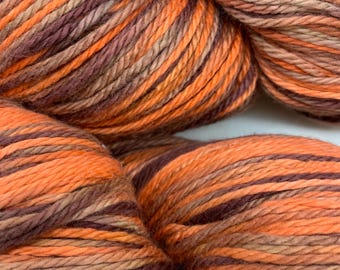 Könnte beinhalten: Nahaufnahme eines Garnknäuels in Orange-, Braun- und Beigetönen. Das Garn hat ein meliertes Aussehen, wobei die Farben ineinander übergehen. Das Garn ist fest gedreht und eignet sich zum Stricken oder Häkeln.