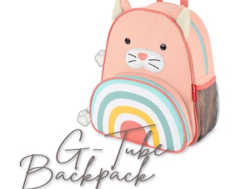 Könnte beinhalten: Ein rosa katzenförmiger Rucksack mit Regenbogenmuster auf der Vordertasche. Der Rucksack hat einen oberen Griff, eine seitliche Netztasche und Katzendetails. Der Text "G-Tube Backpack" steht unten links.