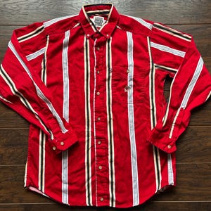 May include: A red, white and black striped long-sleeved button-down shirt with the text "Famous Players Stick" on the front.
