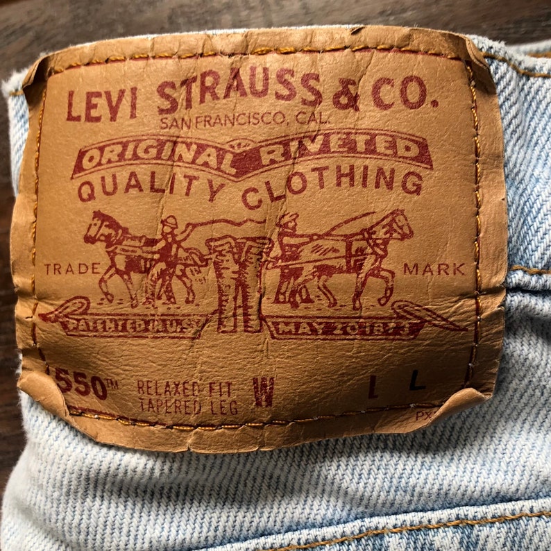 May include: A brown leather Levi Strauss & Co. patch with red stitching. The patch has the text "Levi Strauss & Co. Original Rivited Quality Clothing" and a drawing of two horses pulling a wagon. The text "Trade Mark" is below the drawing. The text "Patented in U.S. May 20 1873" is below the horses. The text "550 Relaxed Fit Tapered Leg" is below the text "Trade Mark". The patch has a size tag that says "W L".
