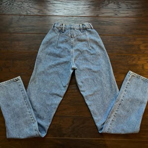 May include: A pair of light blue high-waisted jeans with a button fly and belt loops. The jeans have a straight leg and are made of a soft denim fabric.
