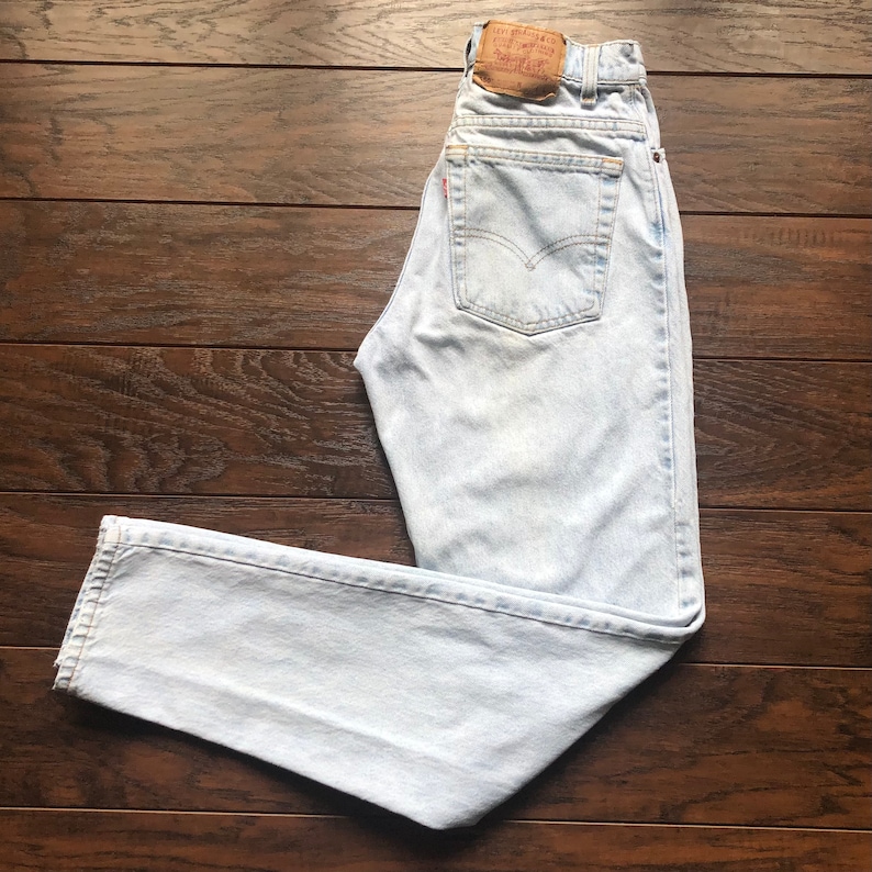 May include: Light blue denim jeans with a brown leather Levi's patch on the back waistband. The jeans have a straight leg and a high waist.