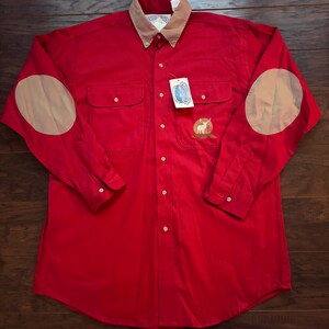 May include: A red long-sleeved button-down shirt with a tan collar and tan elbow patches. The shirt has a small embroidered logo on the left chest.