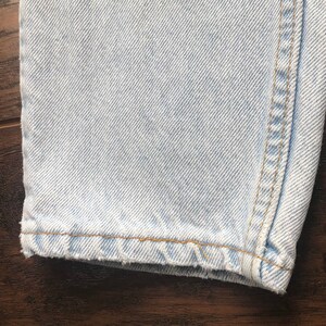 May include: Close-up of the hem of light blue denim jeans with a raw edge and a single stitch of light brown thread.