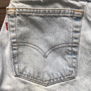 May include: A close-up of a light blue denim back pocket with brown stitching detail. The pocket has a small red Levi's patch on the top left corner.