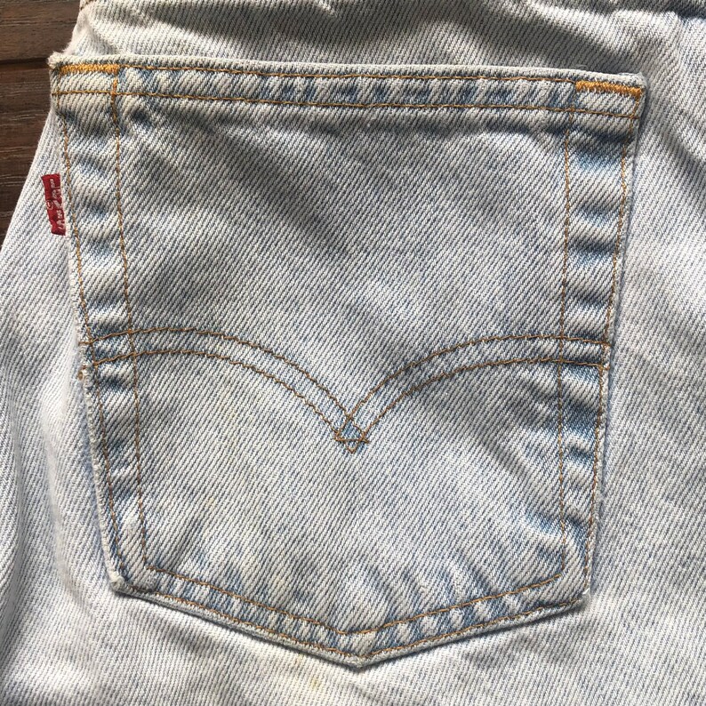 May include: A close-up of a light blue denim back pocket with brown stitching detail. The pocket has a small red Levi's patch on the top left corner.