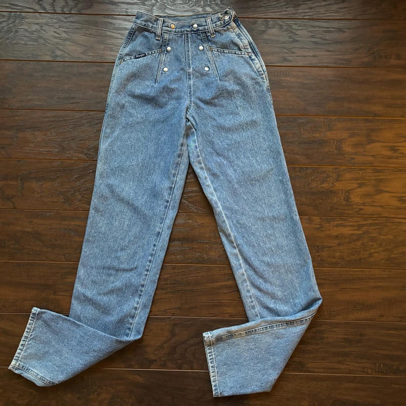 May include: Light blue high-waisted jeans with a button fly and silver buttons. The jeans have a straight leg and are made of a soft denim fabric.