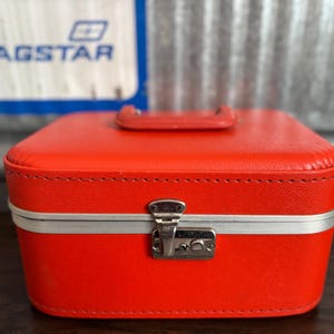 May include: A bright red vintage travel case with a silver latch and trim. The case has a stitched design and a white interior.