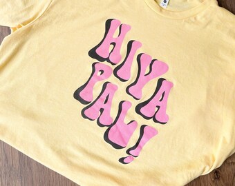 May include: Yellow t-shirt with a pink and black graphic that says "Hiya Pal!"