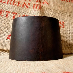 May include: A dark brown leather hat with a wide brim. The hat is sitting on a burlap background.