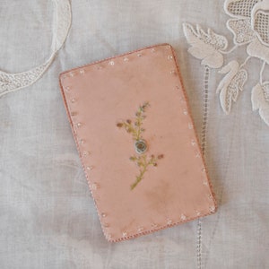 May include: A pink rectangular box with a beaded border and a delicate floral design embroidered on the front.