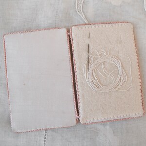 May include: A white needle and thread are inside a pink fabric needle case with a white background.