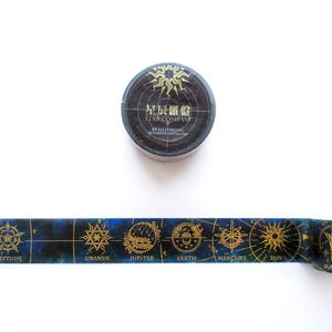 Op de afbeelding: Een rol washi tape met een donkerblauwe achtergrond en gouden accenten. De tape heeft een ontwerp van planeten en sterren met hun namen in gouden letters. De tape is opgerold en het label op de rol staat "星辰羅盤 STAR COMPASS BY SILVERRING VAINGLOFTER COM".
