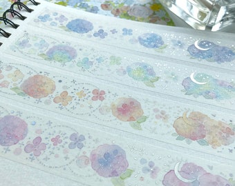 Könnte beinhalten: Ein Blatt dekoratives Washi-Tape mit einem Aquarell-Design aus Hortensien, Blumen und Monden. Das Band ist transparent und hat eine silberne Glitzer-Oberfläche.
