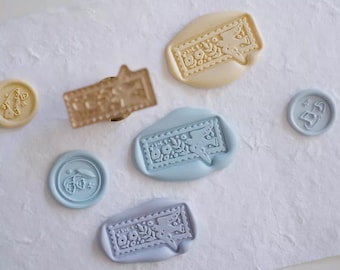 Può includere: Un set di sei sigilli di cera con disegni floreali e di uccelli. I sigilli sono in tonalità di blu e beige. I sigilli sono disposti su una superficie bianca.