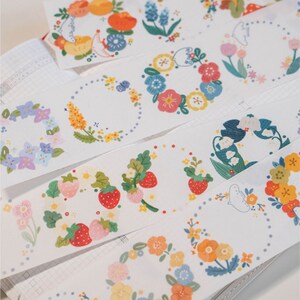 May include: Assortment of colorful washi tapes featuring floral and fruit designs. The tapes are printed on white background and feature wreaths, strawberries, flowers, and other botanical elements.