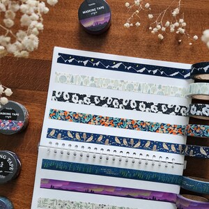 May include: A collection of 10 decorative washi tapes with various patterns and colors, including blue, white, green, and gold. The tapes are arranged on a white page with a spiral binding. The text "Masking Tape" is visible on the top of the page.