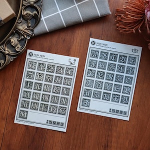 May include: Two sheets of sticker paper with black and white illustrations of numbers and letters. The numbers are in Roman numerals and Arabic numerals. The letters are in a decorative font. The text on the sheets reads "NON-NON It takes all sorts to make a world" and "NON-NON Everything is good in its season".