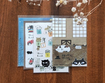 May include: A set of three clear plastic envelopes featuring colourful illustrations of cats and the text "Shinzi Katoh". The envelopes depict a variety of cat designs, including a cat wearing a hat, a cat sleeping, and a cat with a fish.