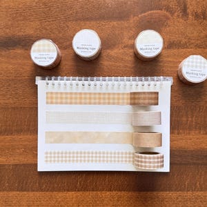 Könnte beinhalten: Vier Rollen Masking Tape mit beigen und braunen Mustern, beschriftet mit Papier Plate Masking tape W 20mm x 7m. Ein Spiralblock zeigt vier Streifen des Klebebands mit großem Vichy-Muster, feinem Gitter, einfarbigem Beige und kleinem Vichy-Muster.