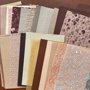 May include: A collection of 20 different textured papers in various shades of brown, beige, and pink. The papers have a variety of patterns, including a grid, a snowflake design, and a crumpled texture.
