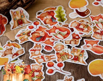 May include: A collection of whimsical stickers featuring woodland creatures like foxes, bears, and rabbits. The stickers have a watercolor style with warm orange, brown, and yellow tones. Designs include mushrooms, houses, and autumn foliage.