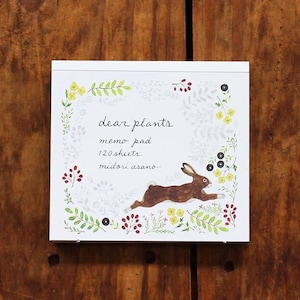 May include: A white memo pad with a brown rabbit running through a field of flowers. The text on the pad reads "dear plants memo pad 120 sheets midori asano".