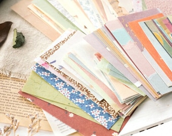 May include: A collection of decorative paper sheets in various colors and patterns. The papers include floral, watercolor, and abstract designs. Some sheets have patterned borders. The papers are arranged on a neutral background with a vintage book.
