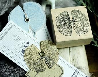 May include: A collection of craft supplies featuring a wooden stamp with a bow design, paper tags, and decorative paper bows in blue and tan. The items are arranged on a textured gray surface, suggesting a vintage or scrapbooking theme.